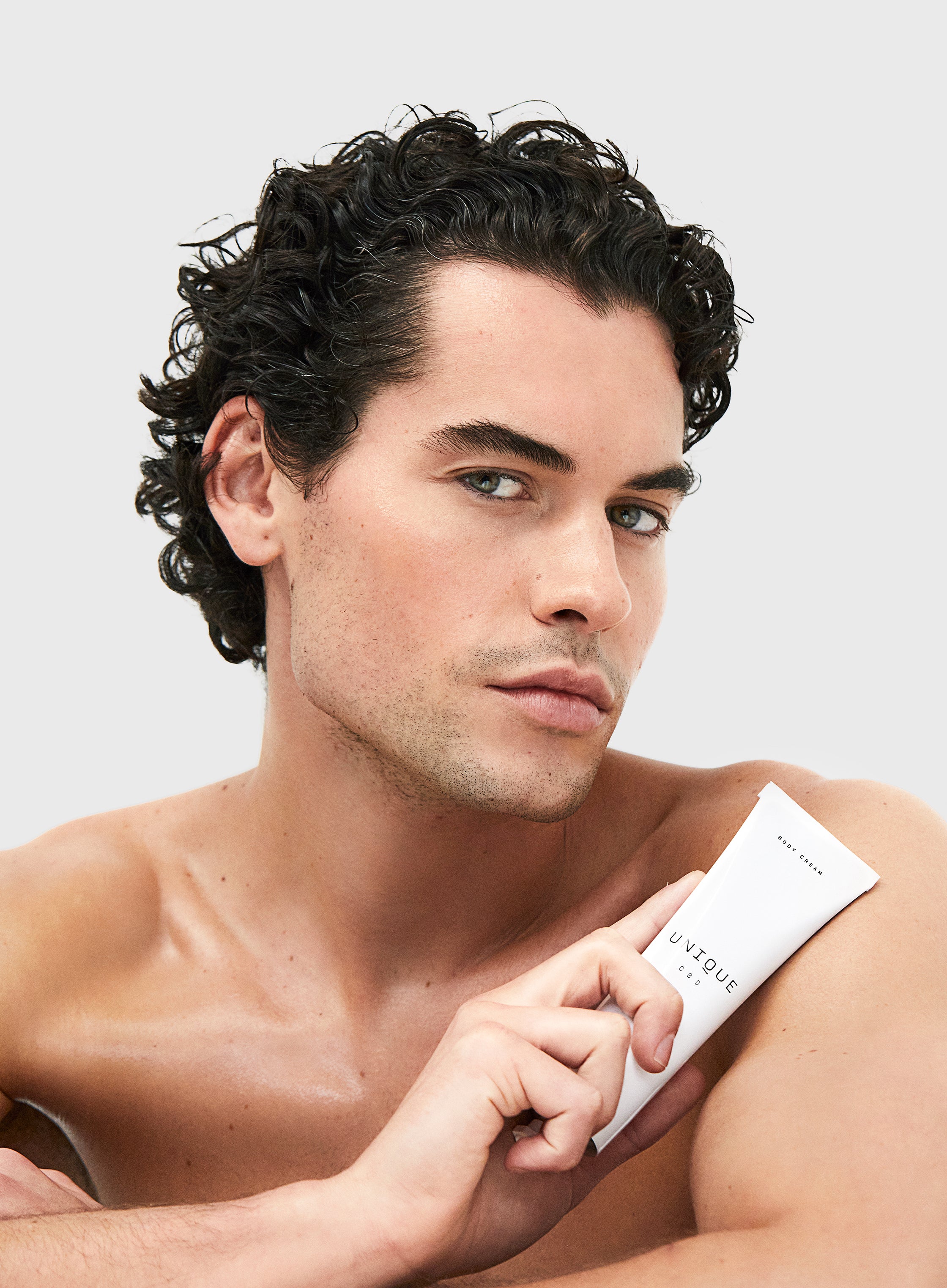 man holding unique cbd body cream tube to his shoulder